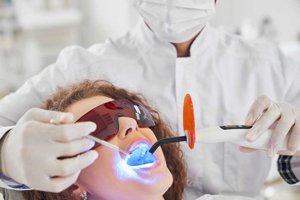Person brushing teeth beside a bathroom sink with a toothbrush, toothpaste, and glass of water