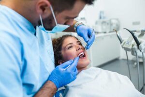A dental hygienist cleaning an adult patient's teeth using professional dental tools in a bright exam room.